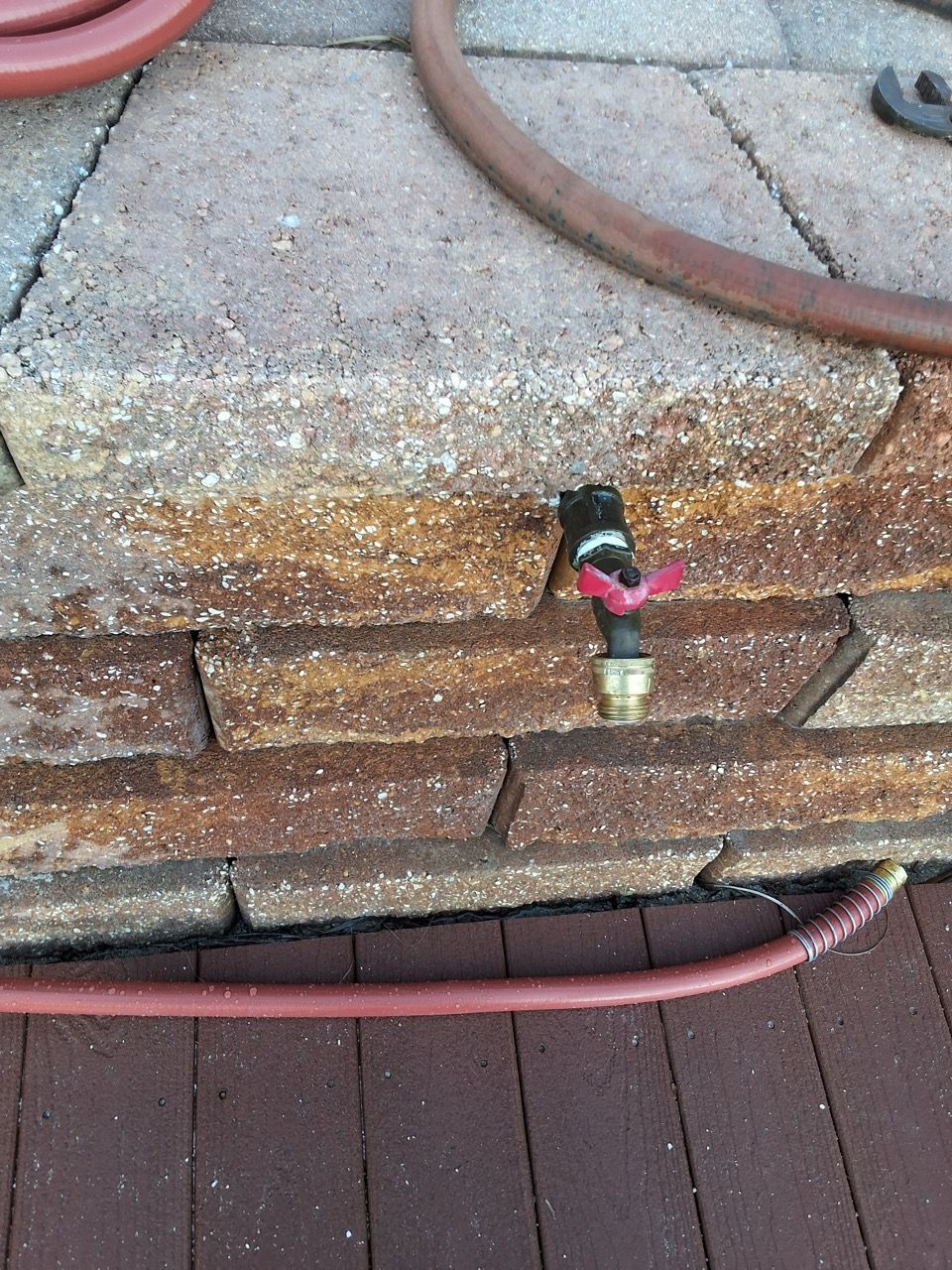 Sprinkler valve and hose on stacked pavers beside a wooden deck