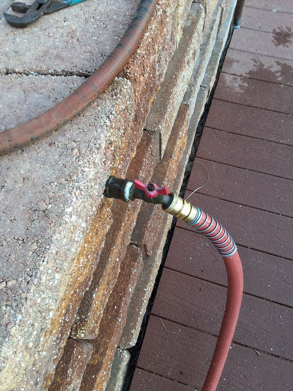 Rusty hose connection on a weathered wooden surface next to a red hose.