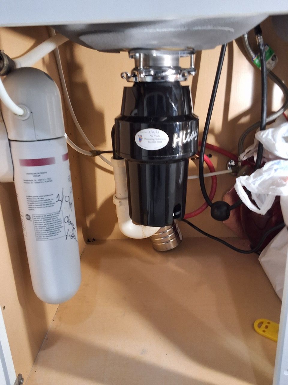 Under-sink plumbing with a black garbage disposal and a white water filter canister