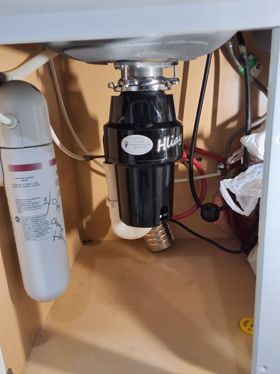 Under-sink garbage disposal with plumbing and a white filter canister underneath a sink