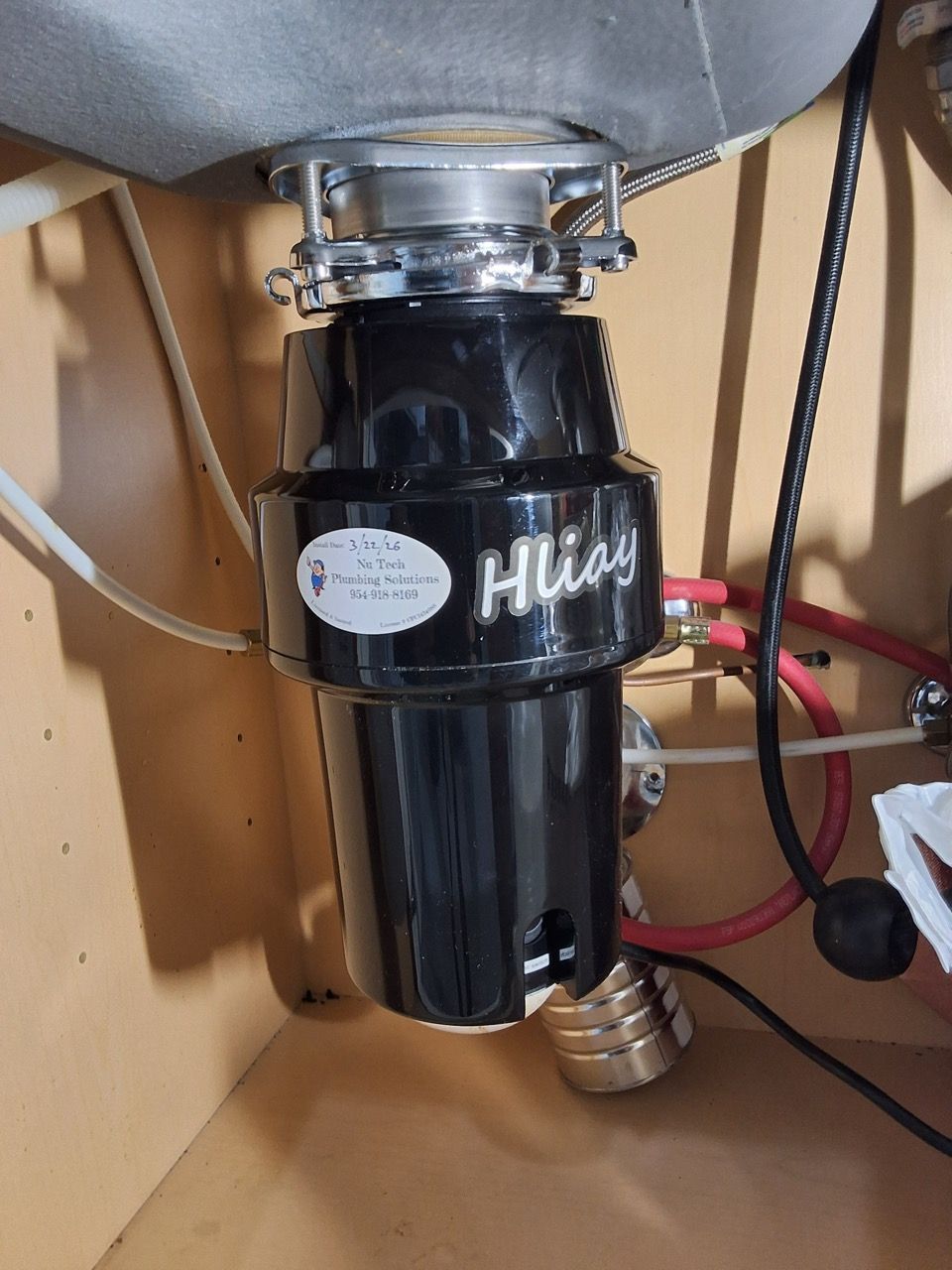 Black garbage disposal under a kitchen sink with pipes and red water lines