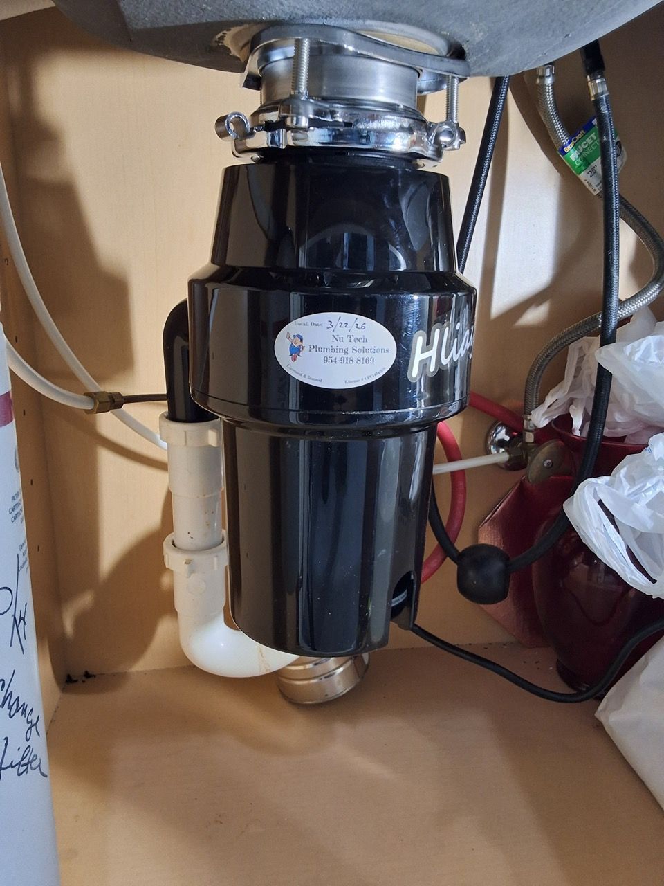 Under-sink garbage disposal unit with black motor housing and white drain pipe connected to a sink.
