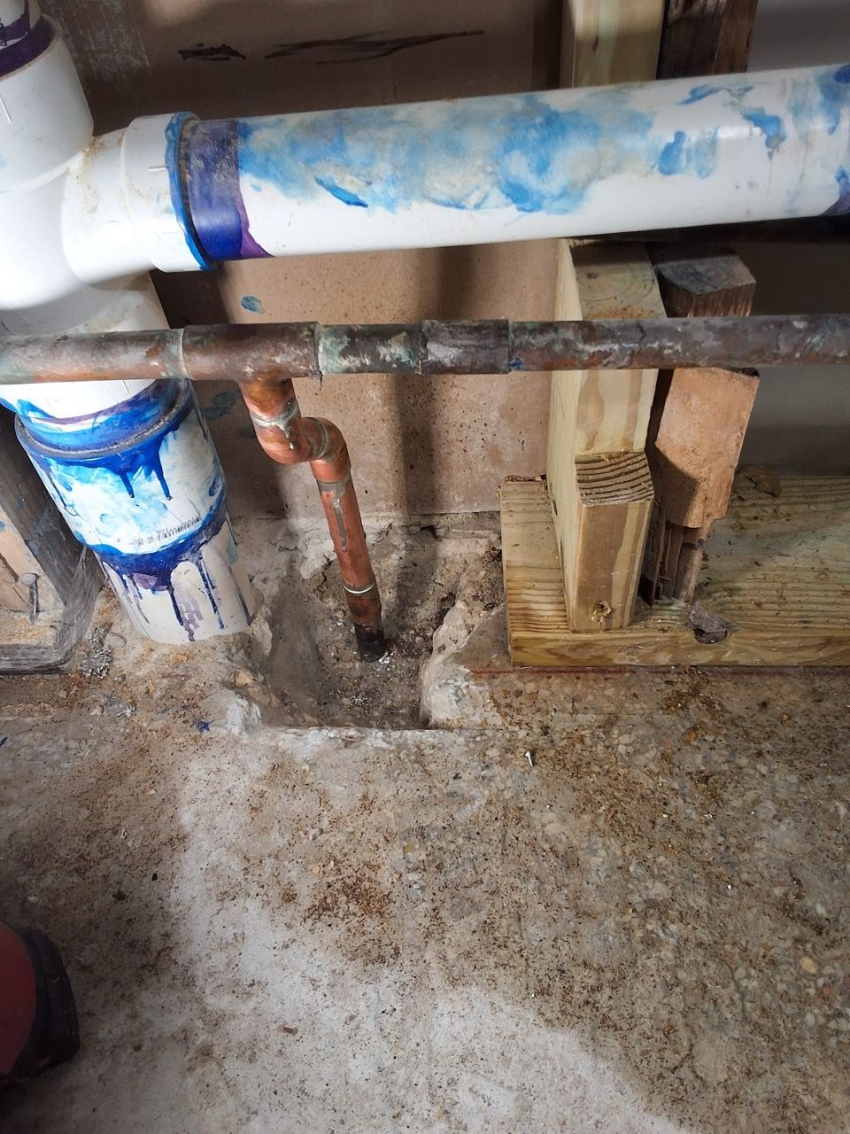Rusty indoor plumbing pipes with peeling blue paint and a concrete floor in a basement-like utility area