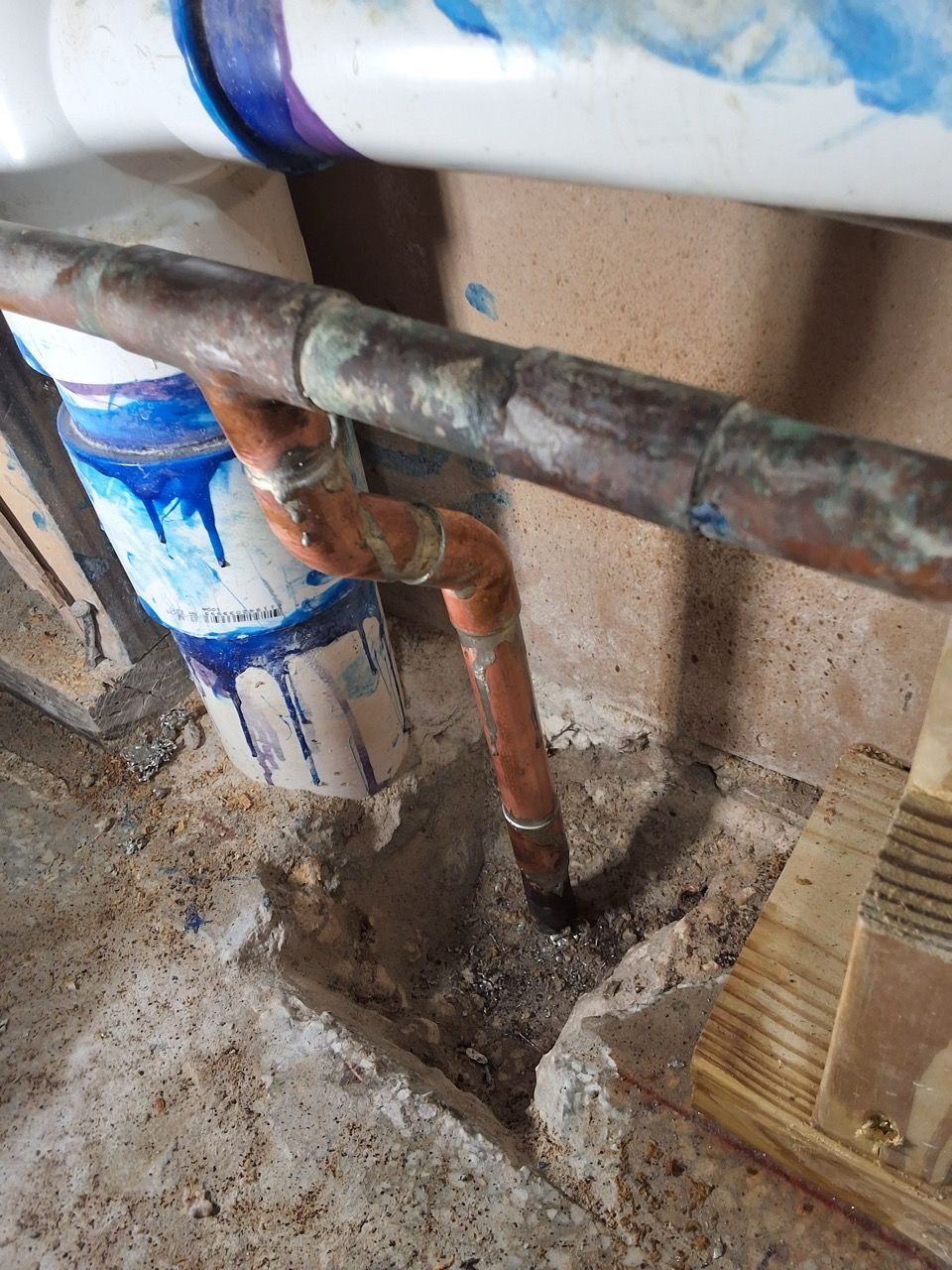 Corroded copper and white pipes under a sink against a wall with blue paint splatters