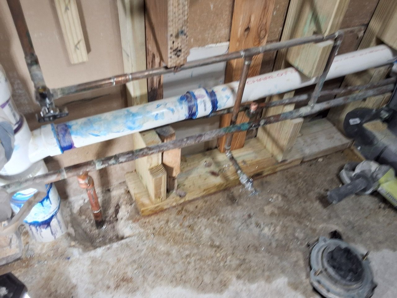 Rough basement wall with exposed pipes, fittings, and construction debris on the floor
