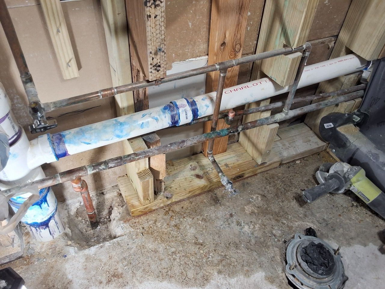 Exposed plumbing pipes and wall framing in a damaged, unfinished interior with debris on the floor.