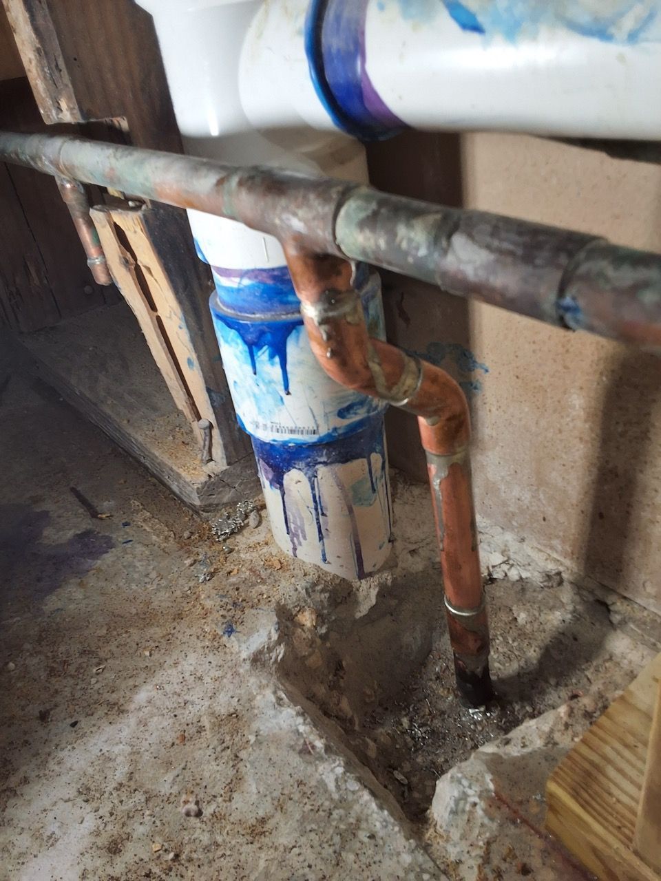 Rusty pipes and a white pipe with blue paint marks in a dusty utility area.