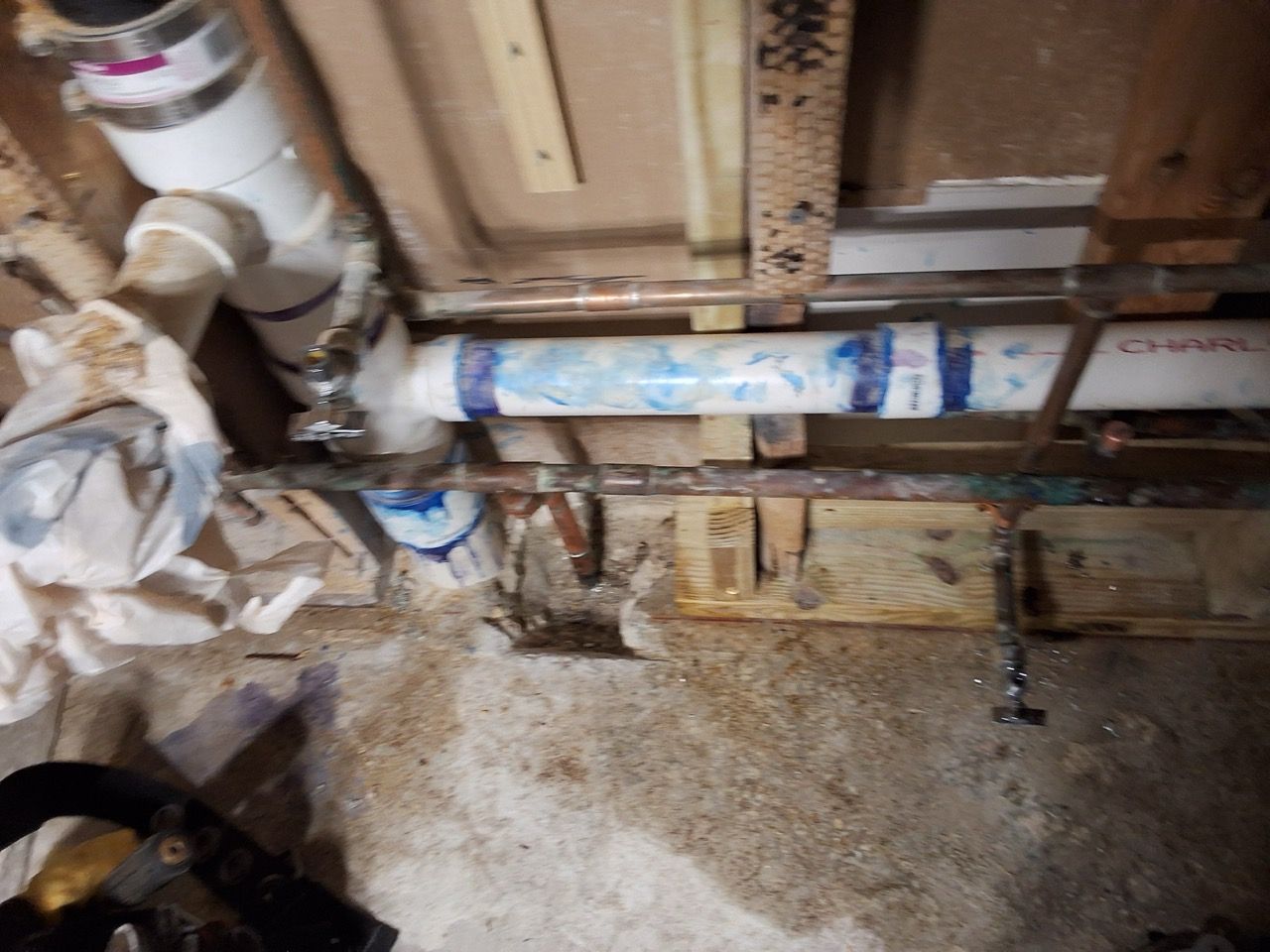 Basement wall with exposed pipes, valves, and stained concrete floor during plumbing work
