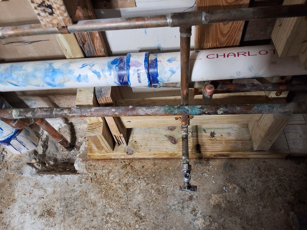 Rusty pipes and a valve under a wooden floor, with a white pipe labeled in red.