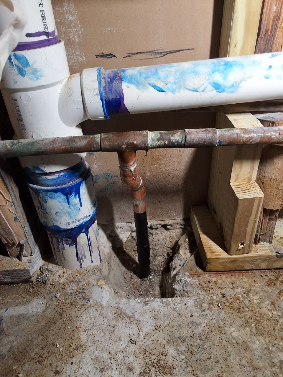 Close-up of exposed plumbing pipes with blue primer and a rusted valve in a construction area.