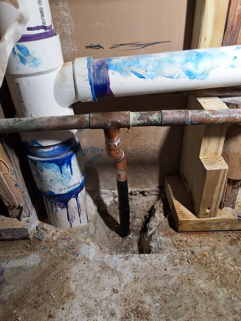 Rusty pipes and a white-painted plumbing setup with blue paint marks in a basement-like utility area.