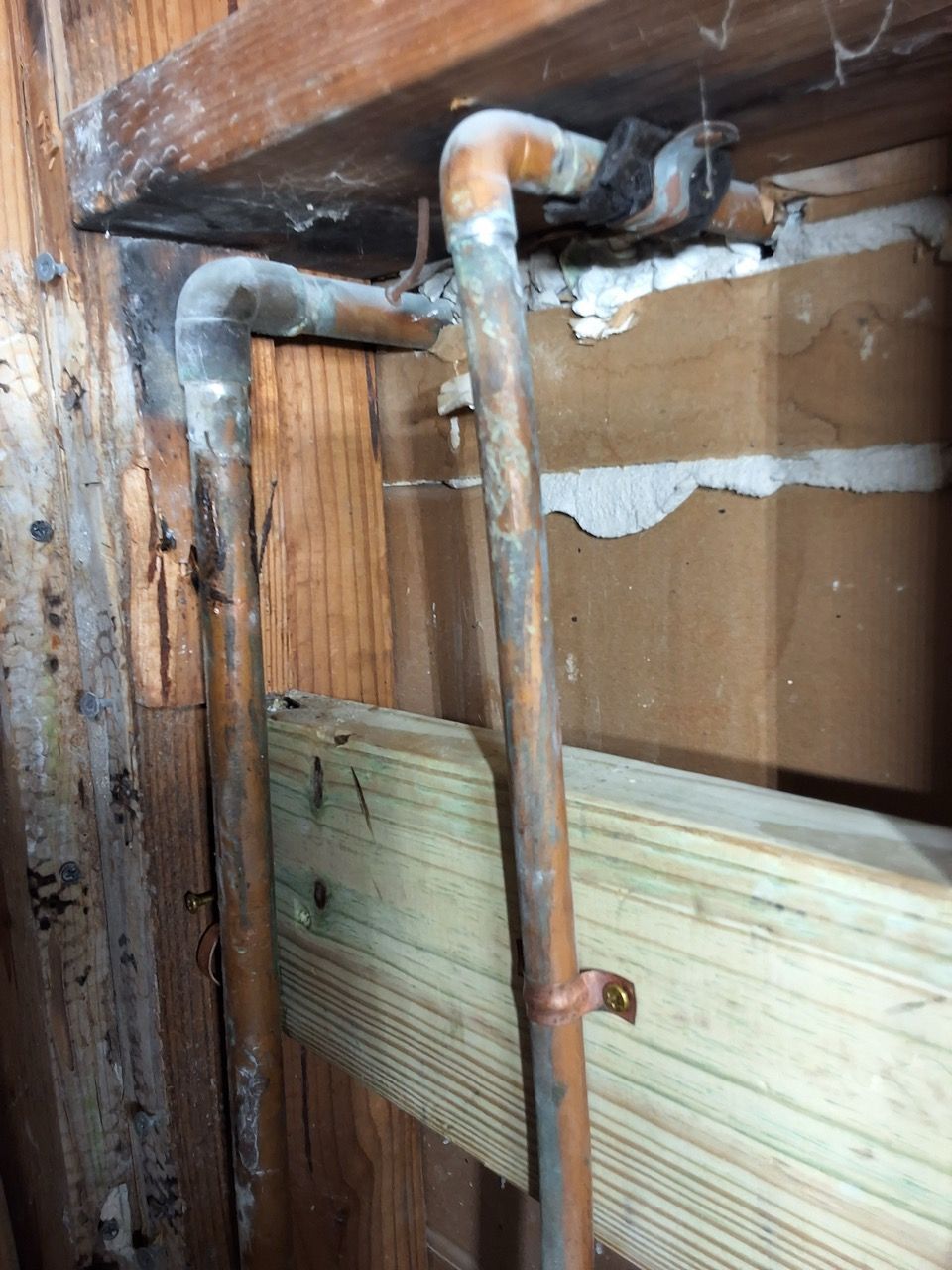 Rusty exposed pipes and damaged wall panels inside a deteriorating room.
