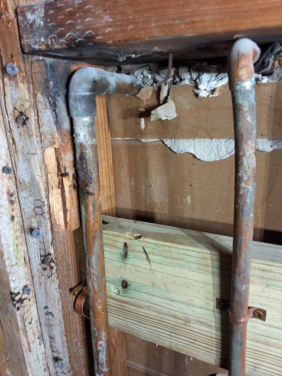 Exposed pipes and wood framing inside a wall cavity with damaged drywall and insulation.