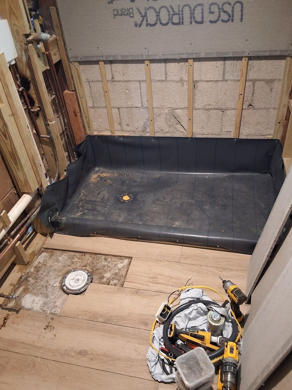 Partially built room with framed walls, a black bench cushion, plywood floor, and construction tools on the floor