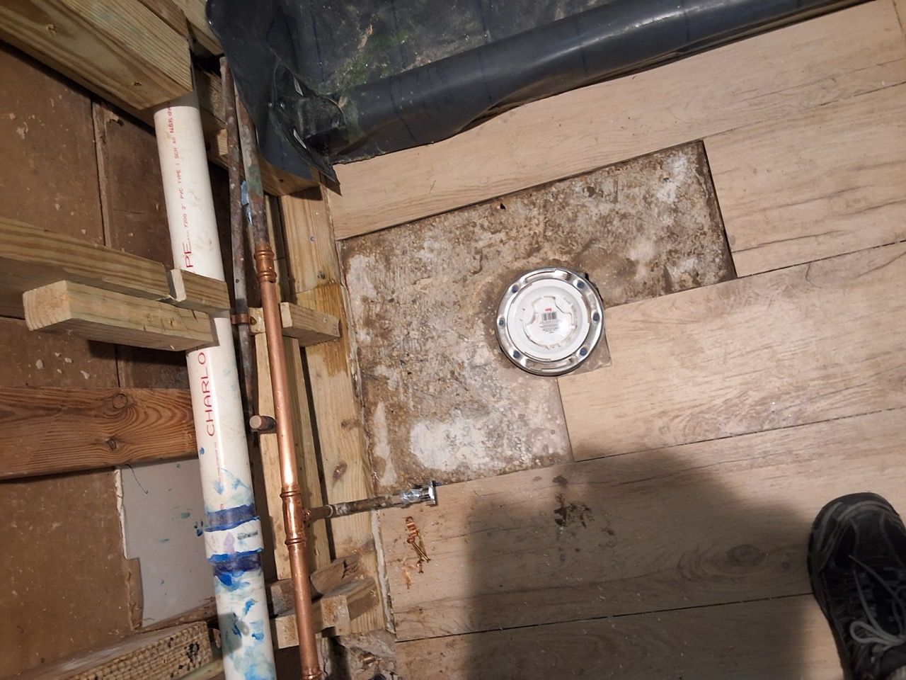 Basement floor with exposed wooden joists, a pipe, and a round floor drain or vent.