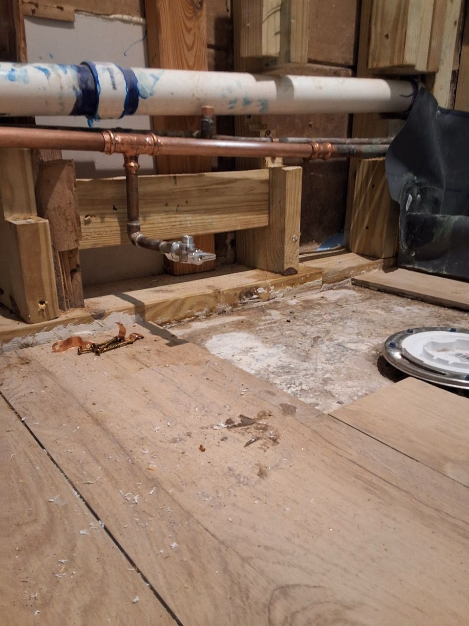 Exposed plumbing and wooden floor in a partially renovated room with dust and debris