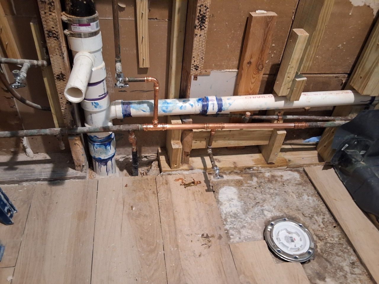 Construction area with exposed PVC pipes, plywood flooring, and a round floor drain.