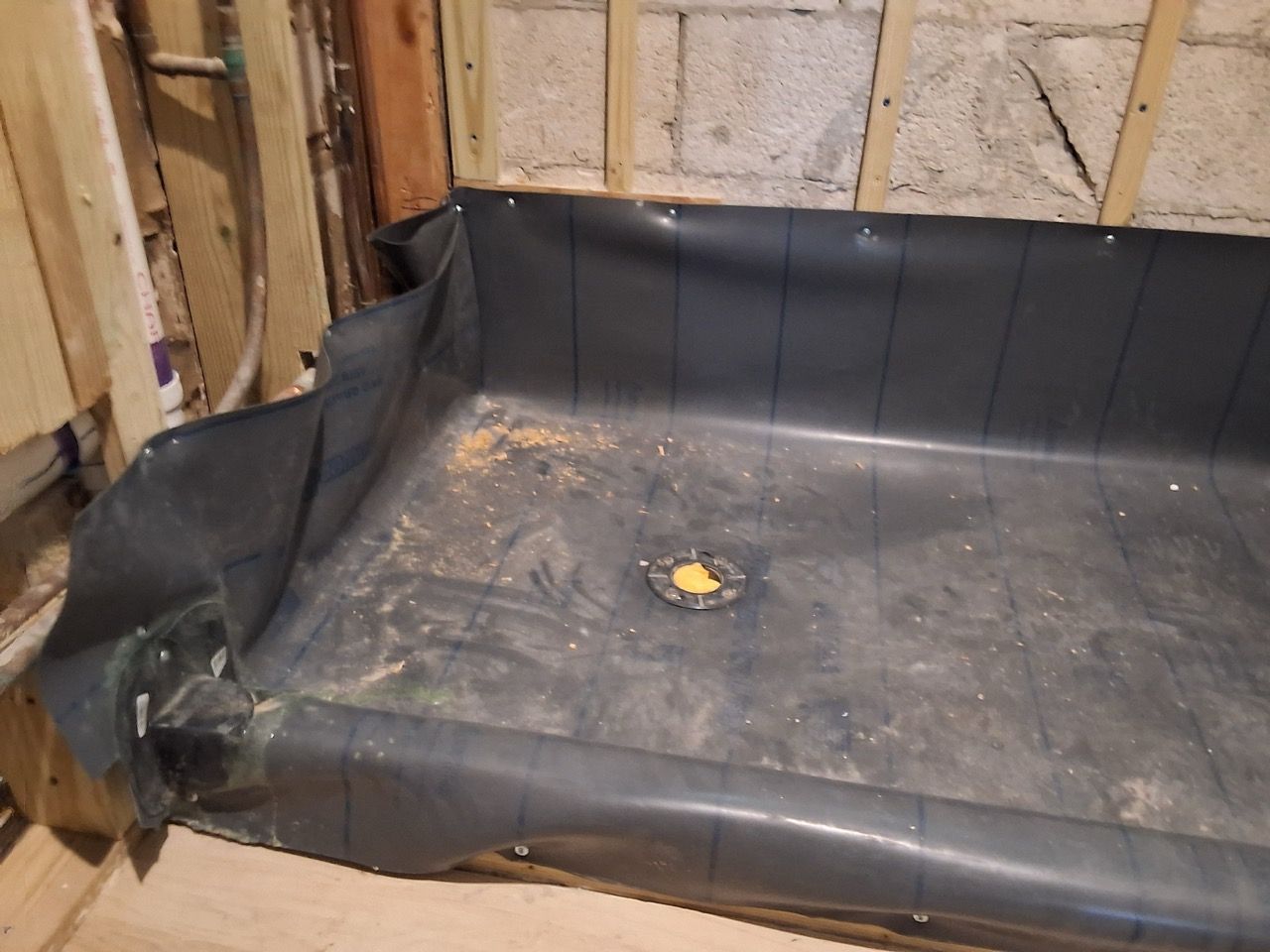 Black waterproof liner in a damaged basement corner with a floor drain.