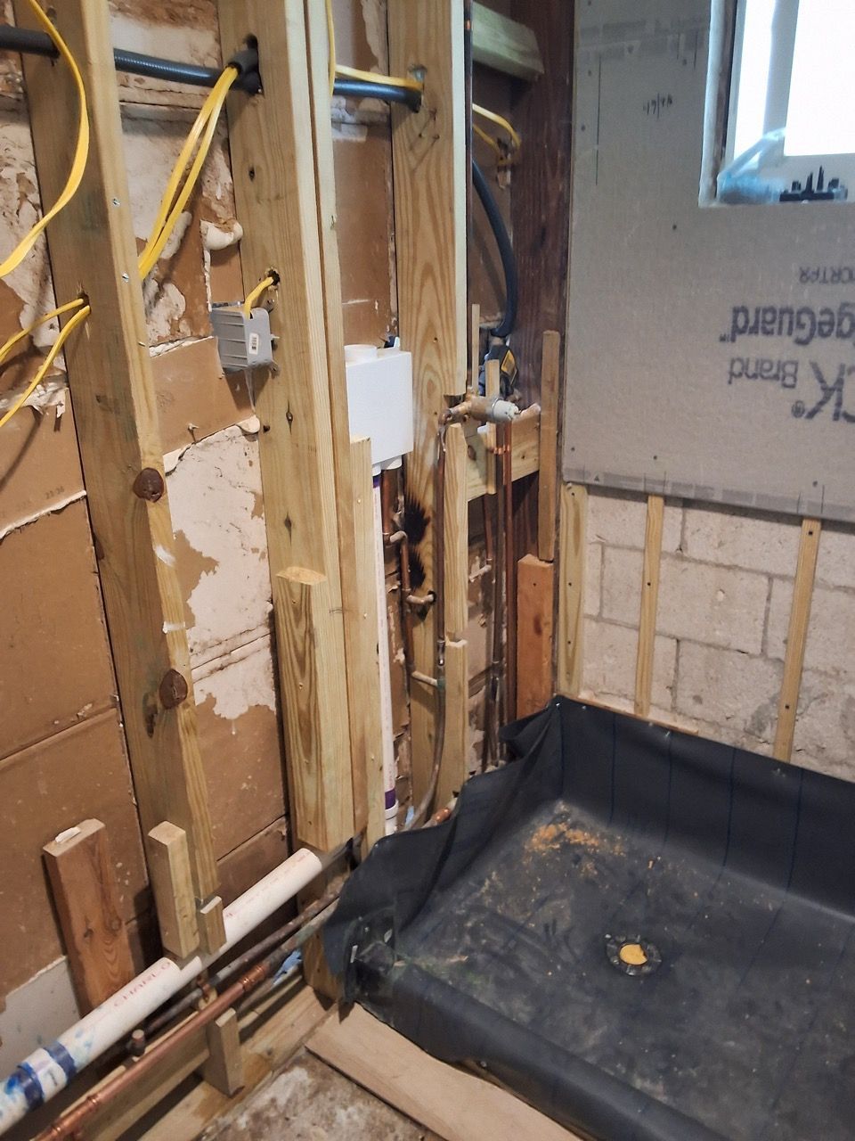 Interior wall under renovation with exposed studs, pipes, insulation, and a black floor liner
