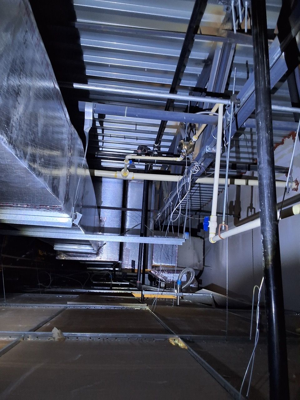 Dark industrial corridor with metal beams, pipes, and reflective floor under dim blue lighting