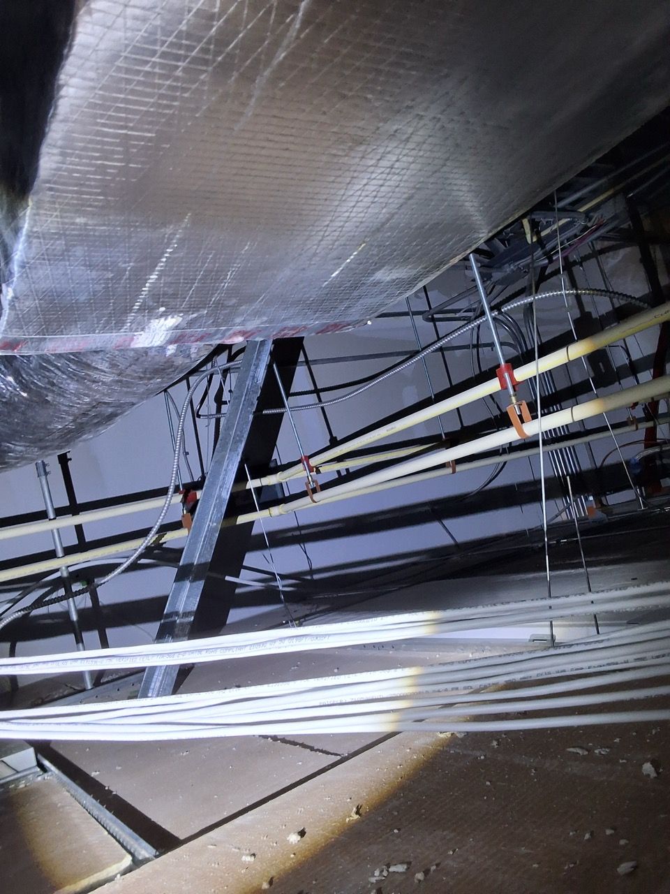 Reflective metal ducting and black support beams inside an industrial ceiling space