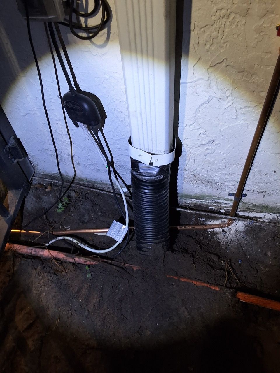 Basement utility area with a white drainpipe and black insulated pipe beside cables on a concrete floor.