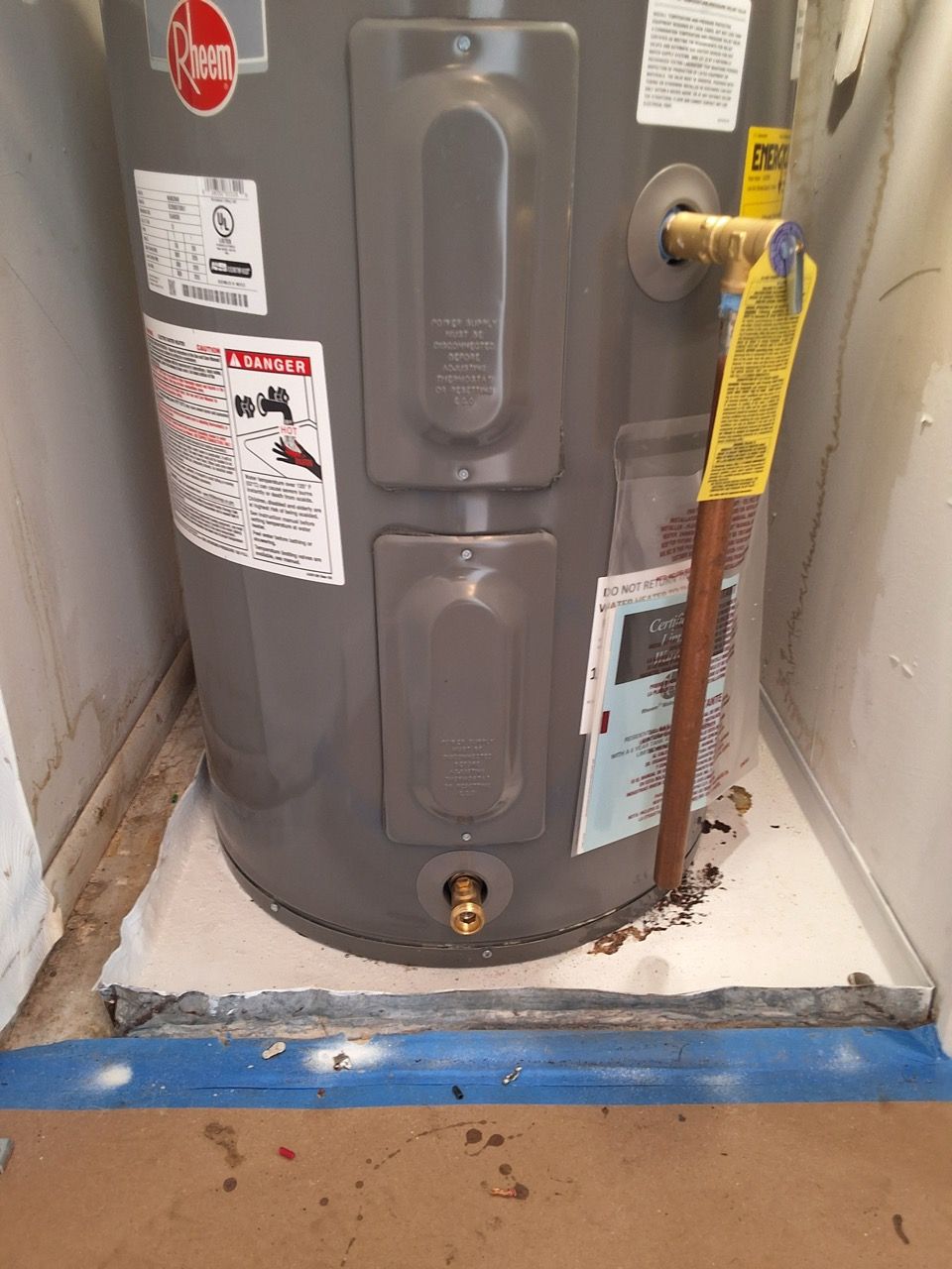 Gray water heater in a tight utility closet with yellow gas shutoff valve and blue floor marking.