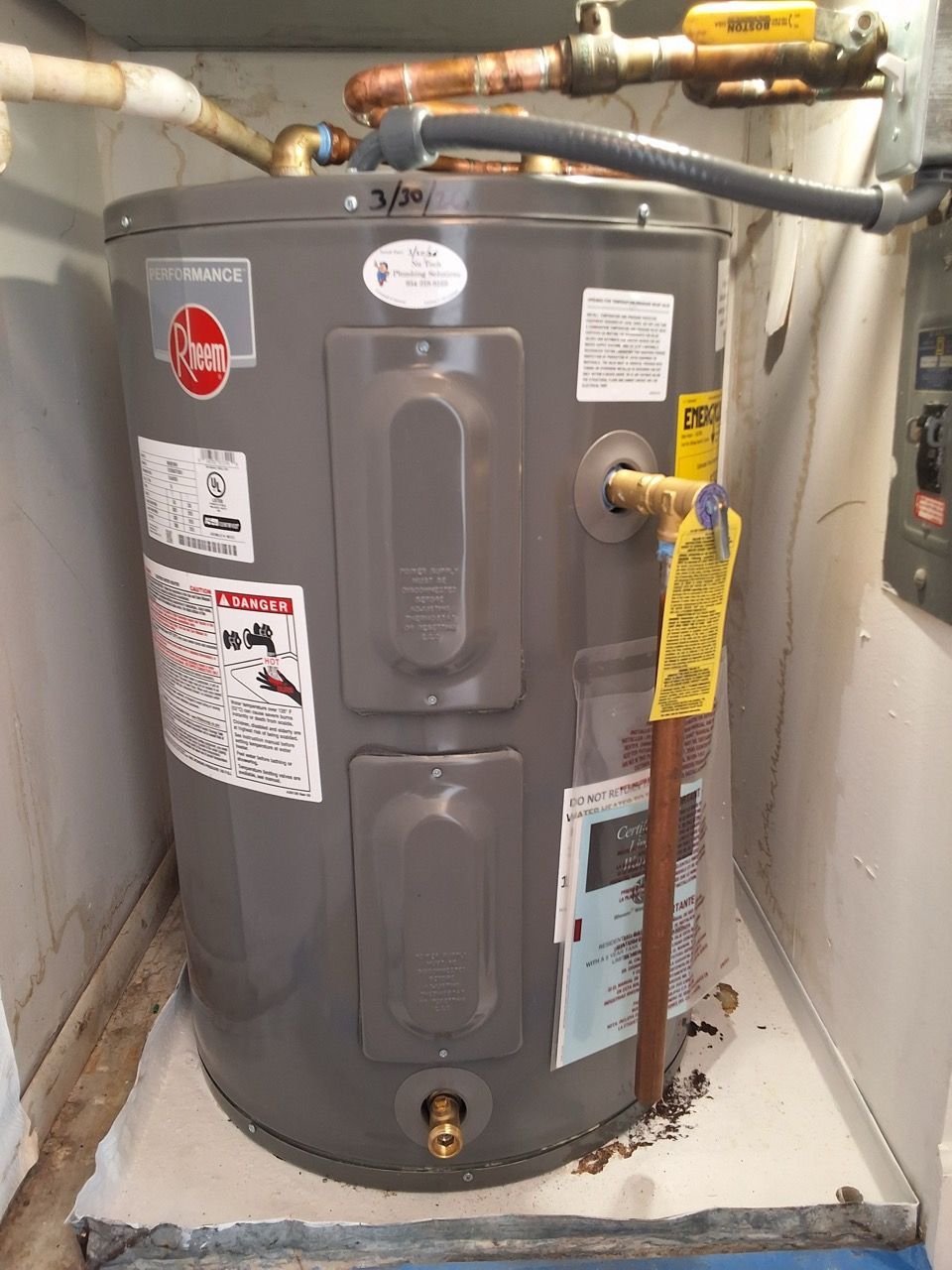 Gray water heater with pipes and a yellow gas shutoff valve in a utility room.