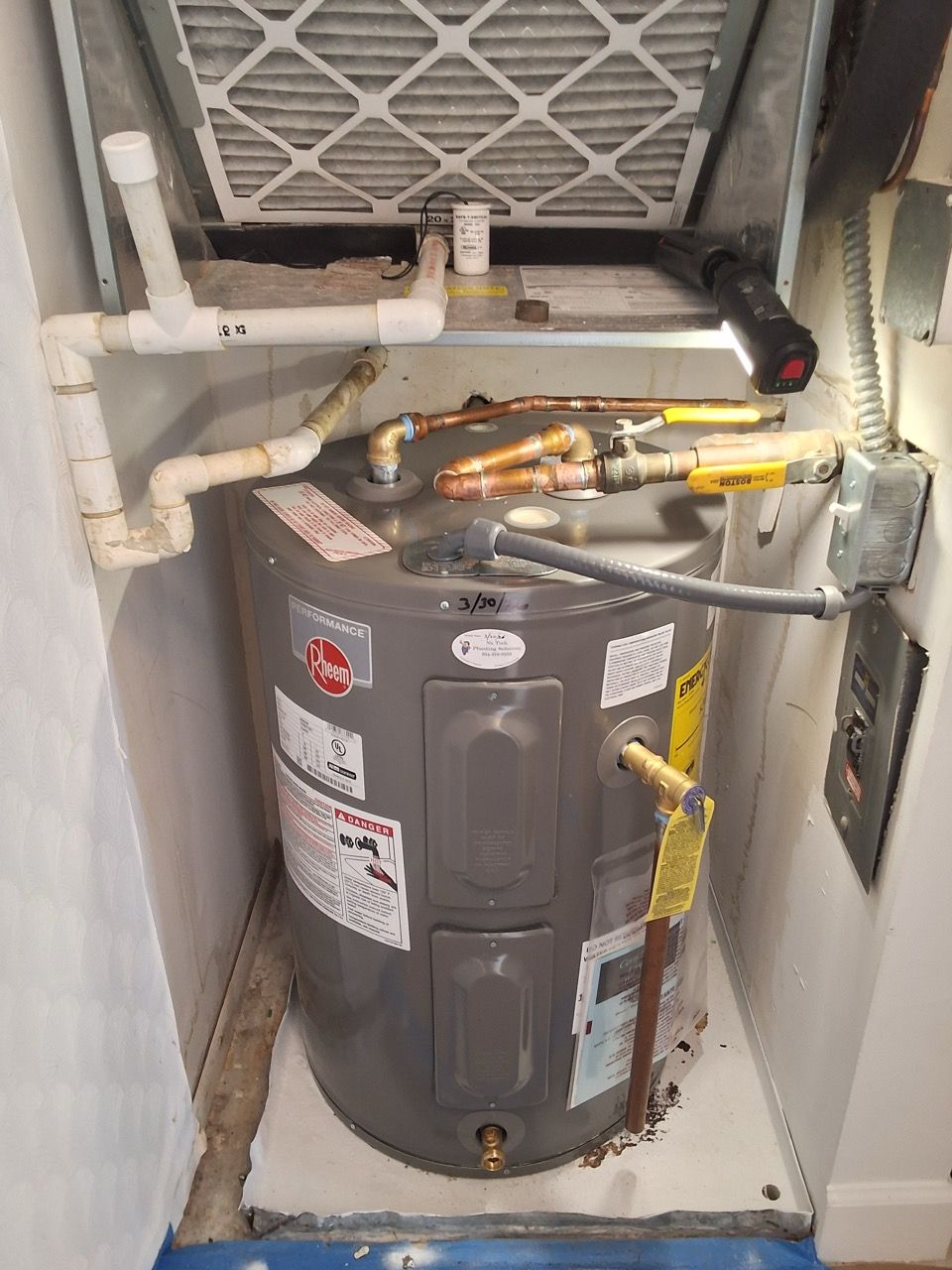 Water heater in a cramped utility closet with exposed pipes and ducts.