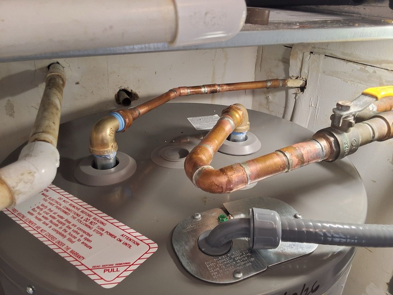 Gas water heater with copper pipes and a flexible hose in a utility area.