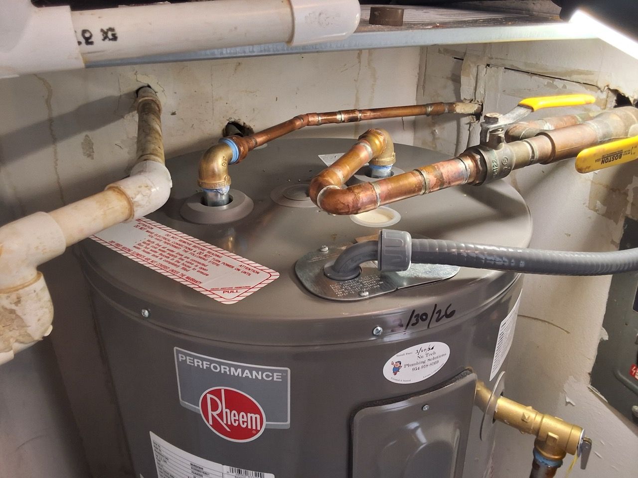 Rheem water heater with copper pipes and hoses in a utility closet