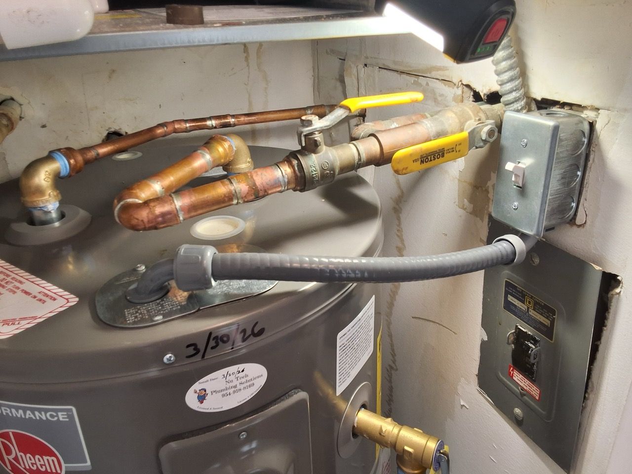 Water heater plumbing and gas connections with copper pipes and yellow shutoff valves in a utility closet
