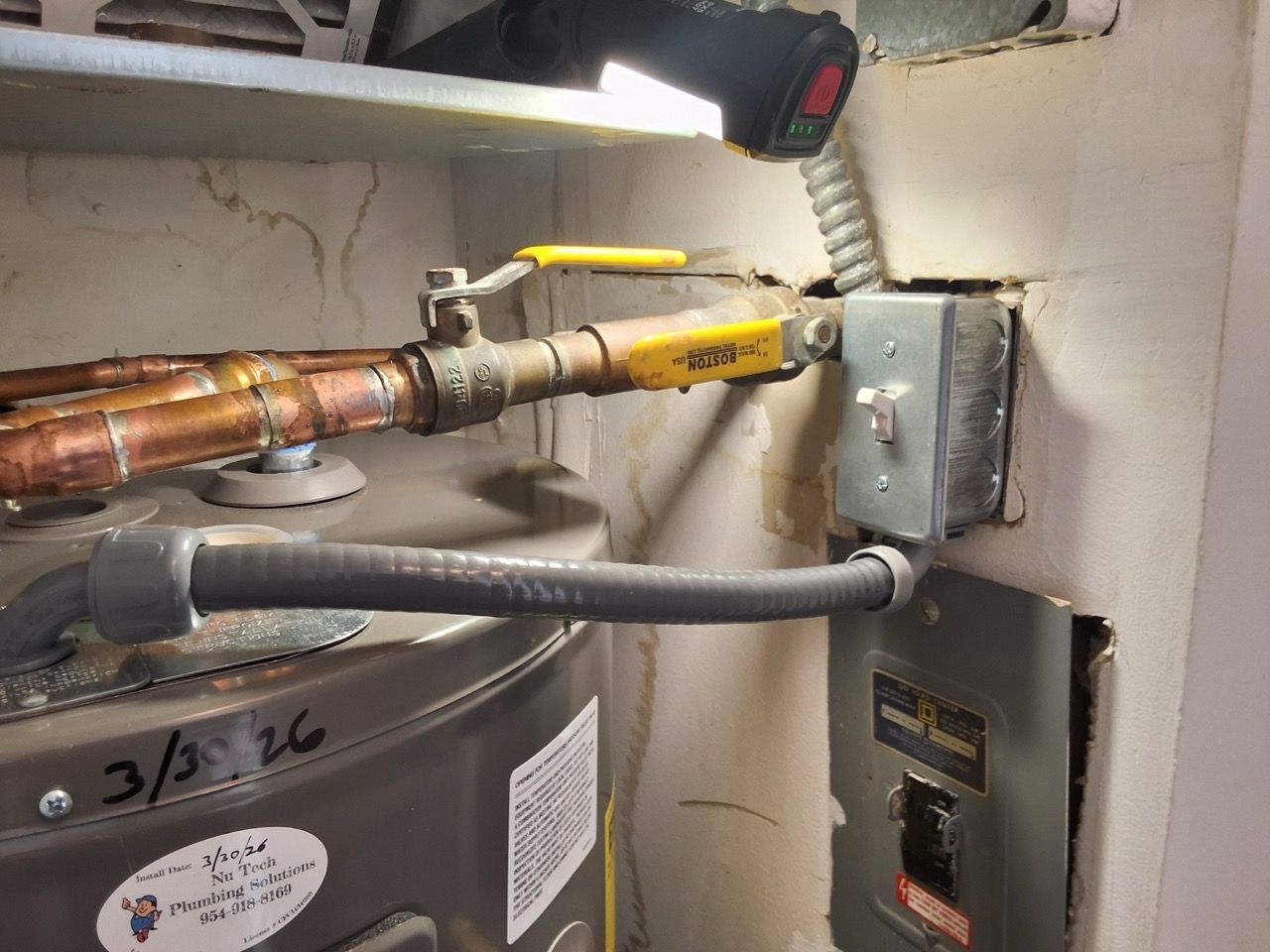 Copper and gray pipes with yellow valve near a furnace control box in a utility room