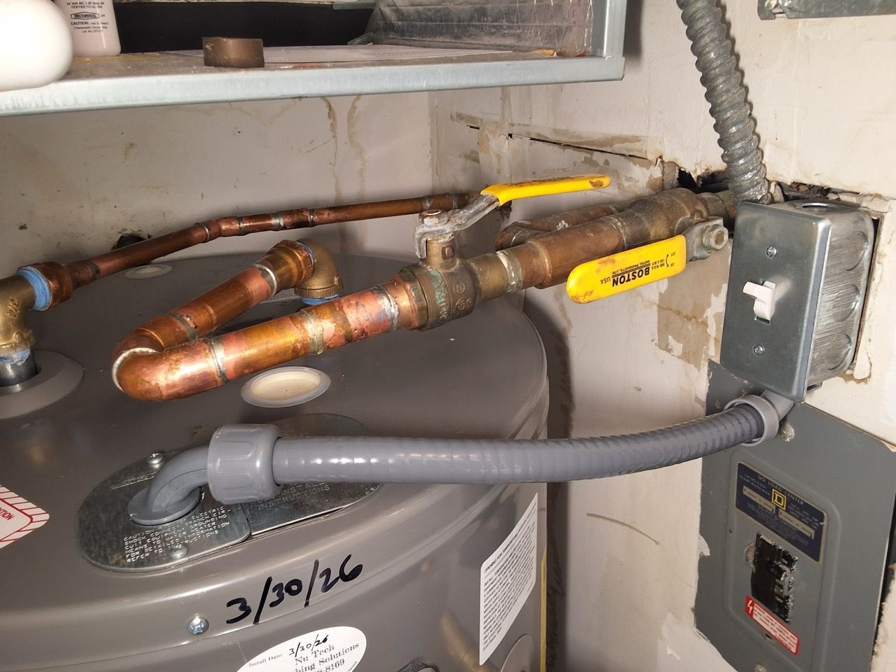 Metal pipes and yellow valve handles in a utility cabinet, with a gray hose and wiring on the right.