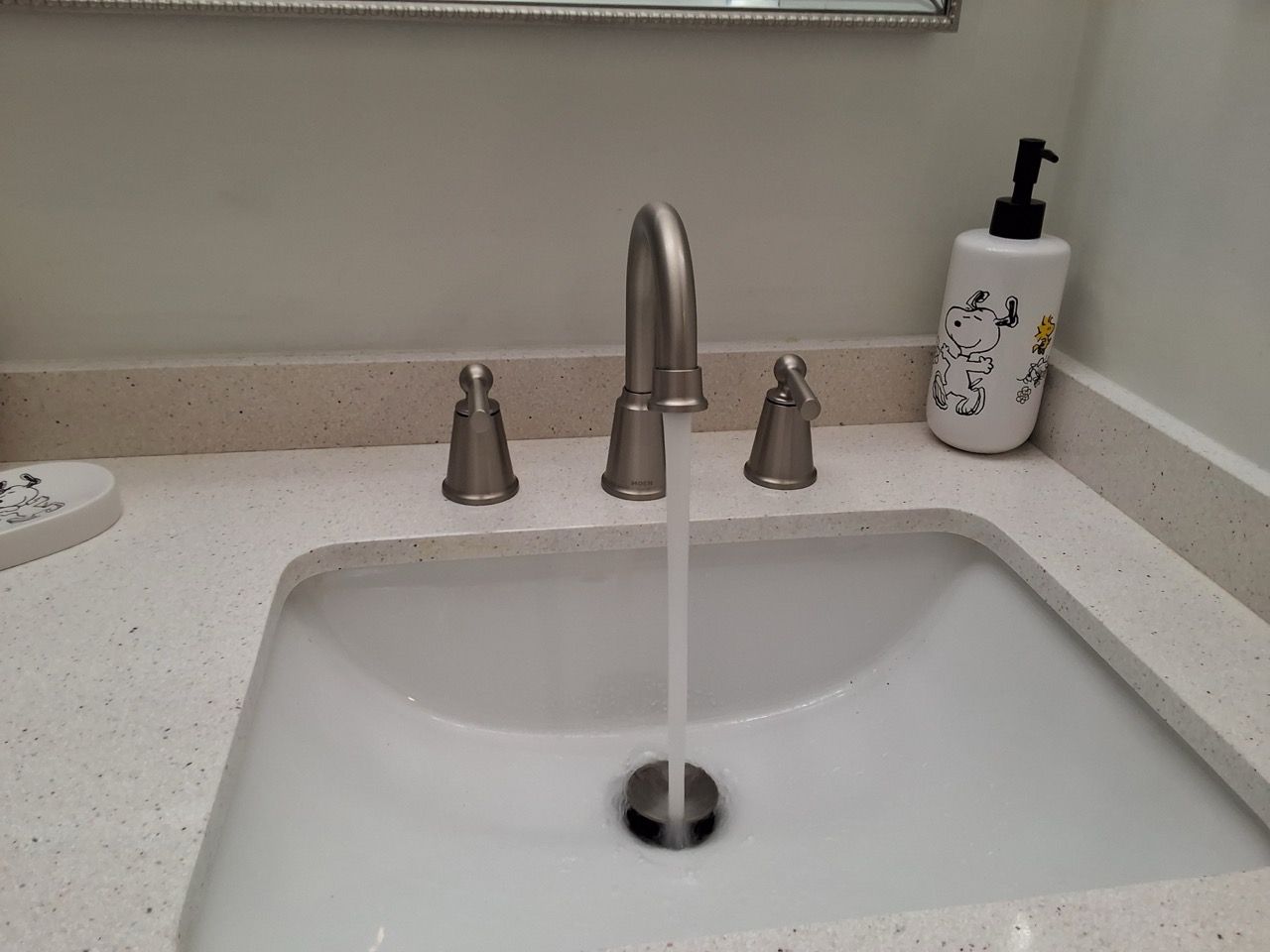 Bathroom sink with running faucet and soap dispenser on the counter