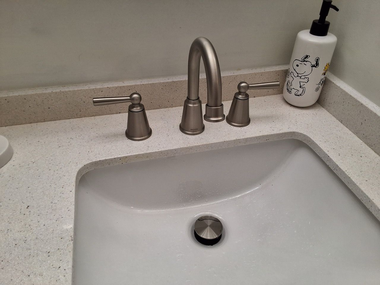 White bathroom sink with chrome faucet and soap dispenser on a speckled countertop.