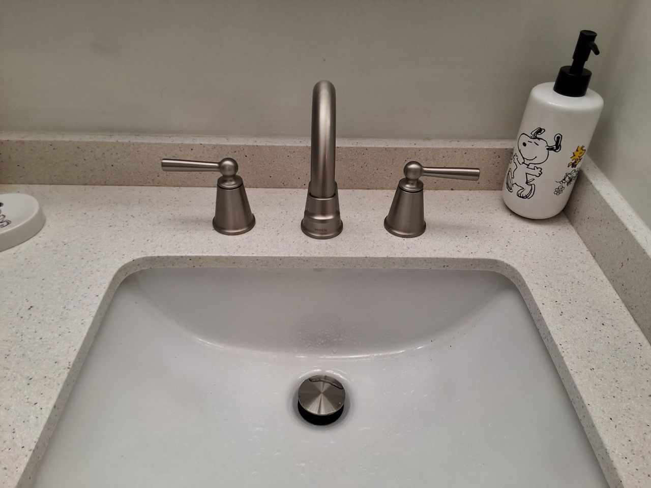 Bathroom sink and chrome faucet on a beige countertop with a soap dispenser.