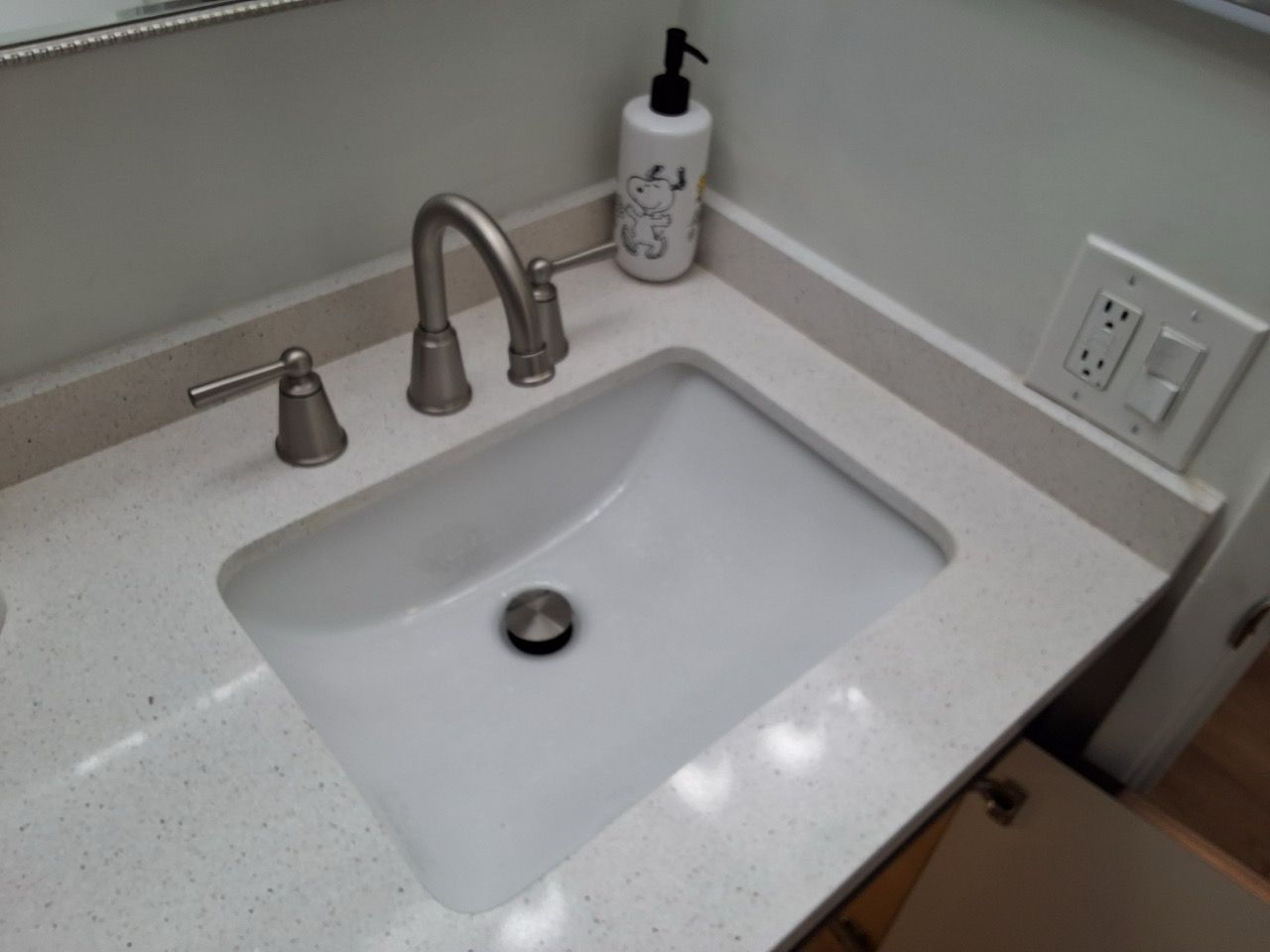 Bathroom sink with chrome faucet, soap dispenser, and wall outlet on a white countertop.