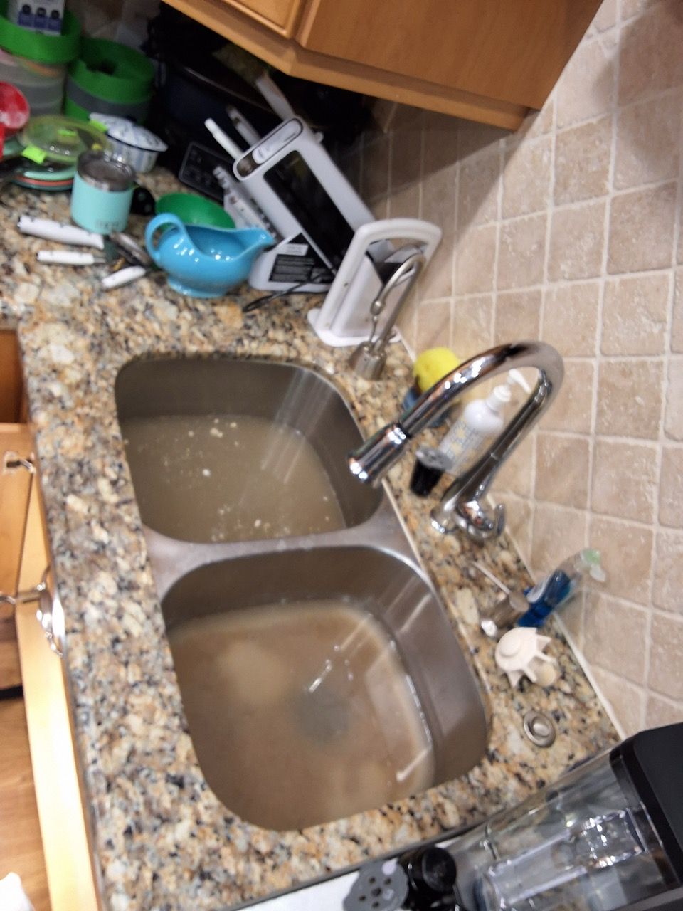 Cluttered kitchen counter with double sink full of dirty water and dishes, tilted toward cabinets.