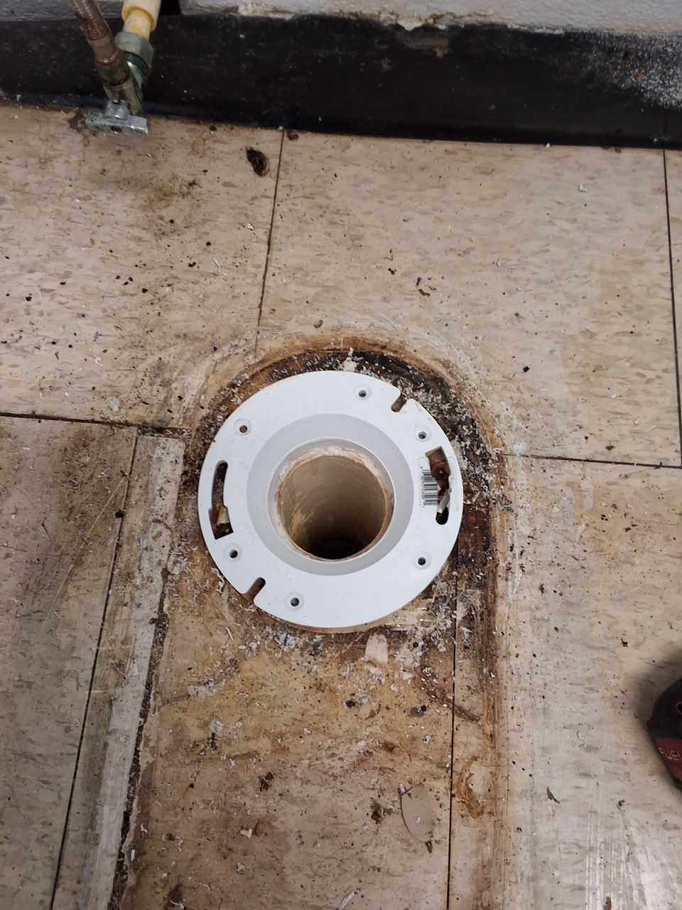White circular floor drain set into a dirty beige tile floor, with rust stains around it.