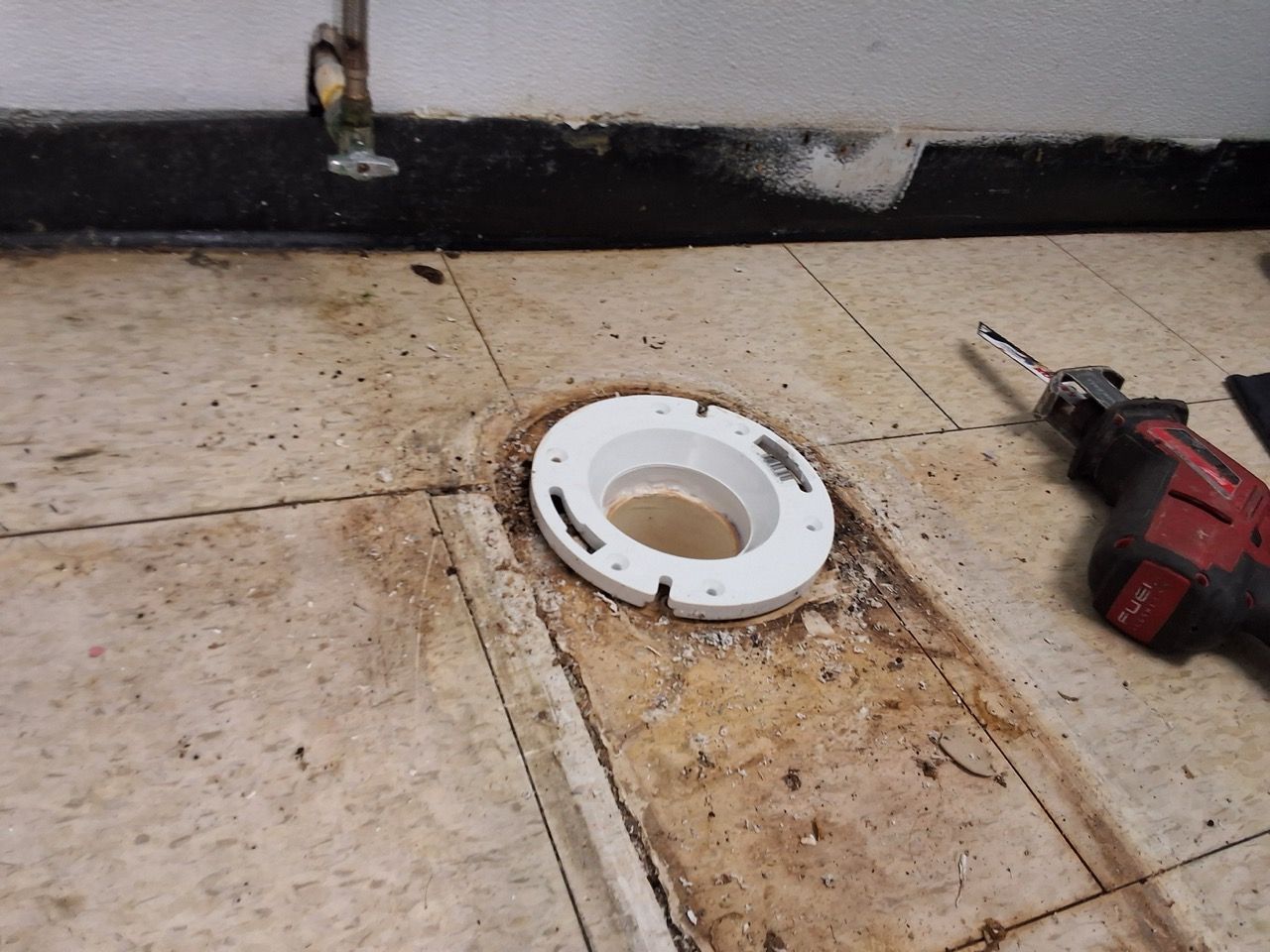 Bathroom floor with a toilet flange opening and a red power drill nearby