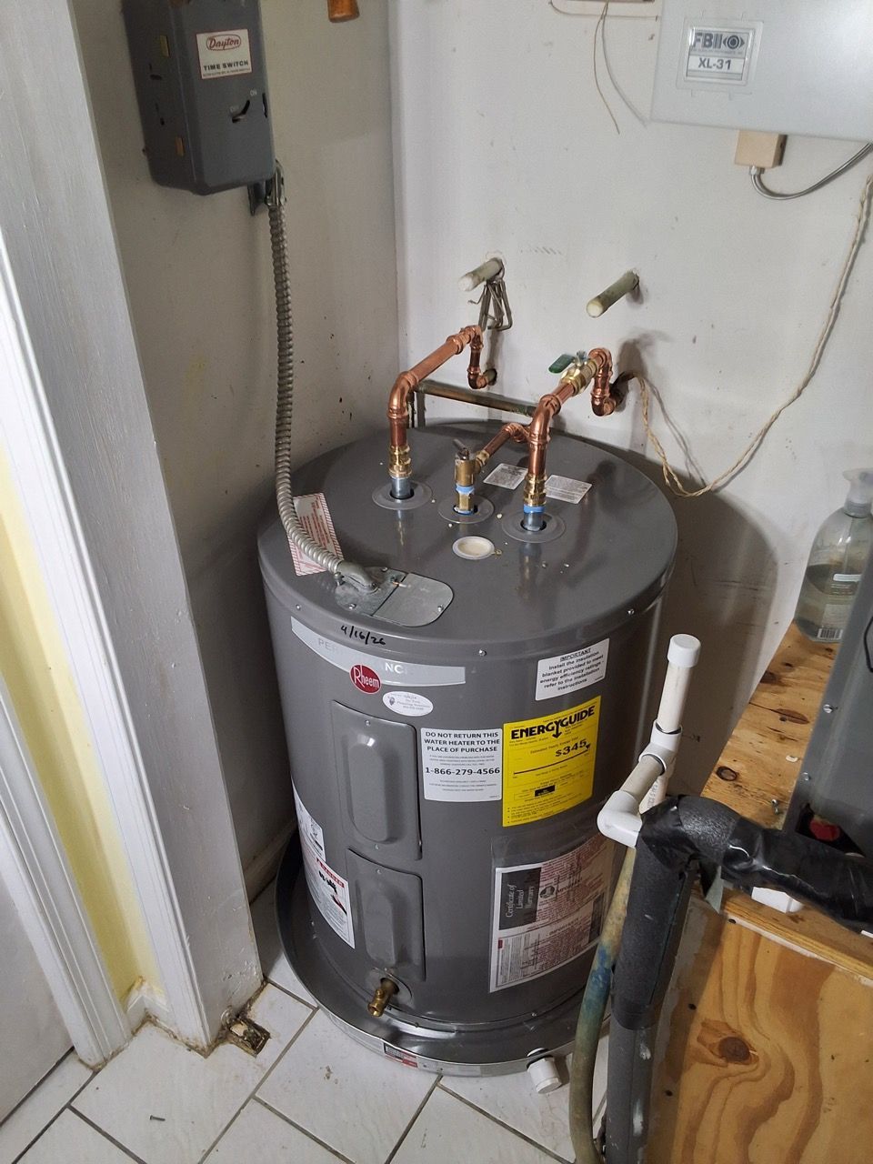 Gray water heater with copper pipes in a utility closet next to a wall and doorway.