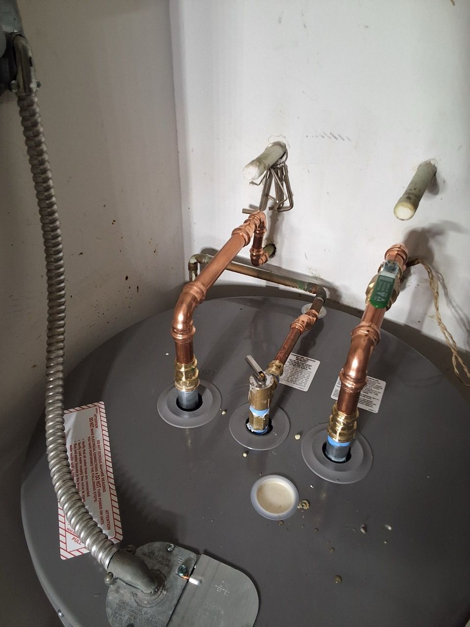 Water heater plumbing with copper pipes and valves above a gray tank in a utility closet.