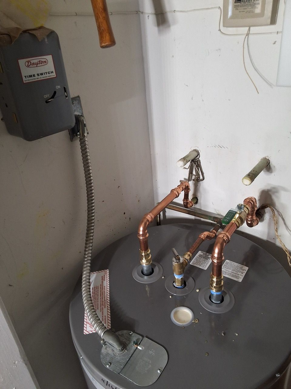 Water heater with exposed copper pipes, valves, and a drain pan in a utility closet.