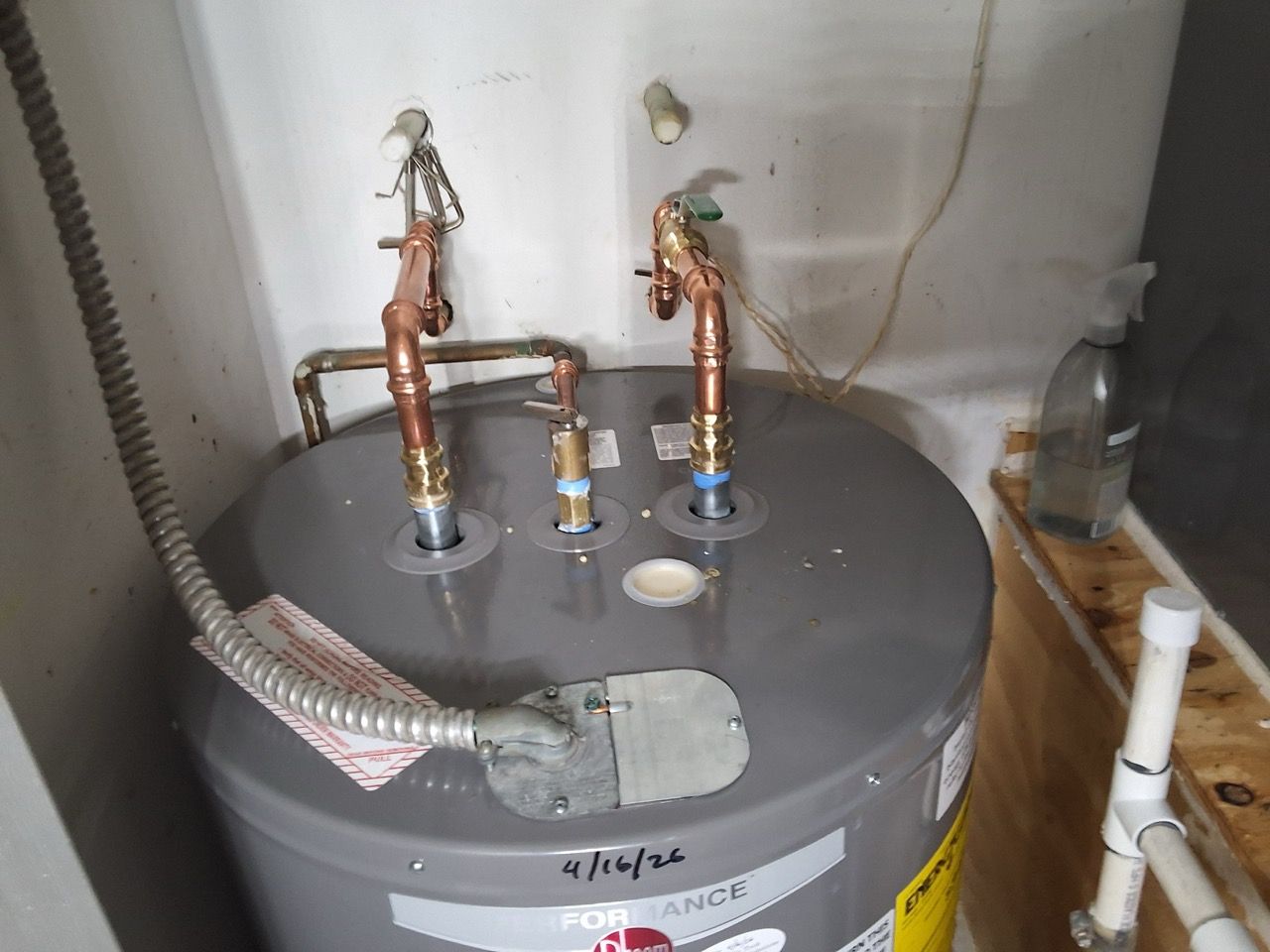 Open water heater with exposed pipes, valves, and wiring in a utility area