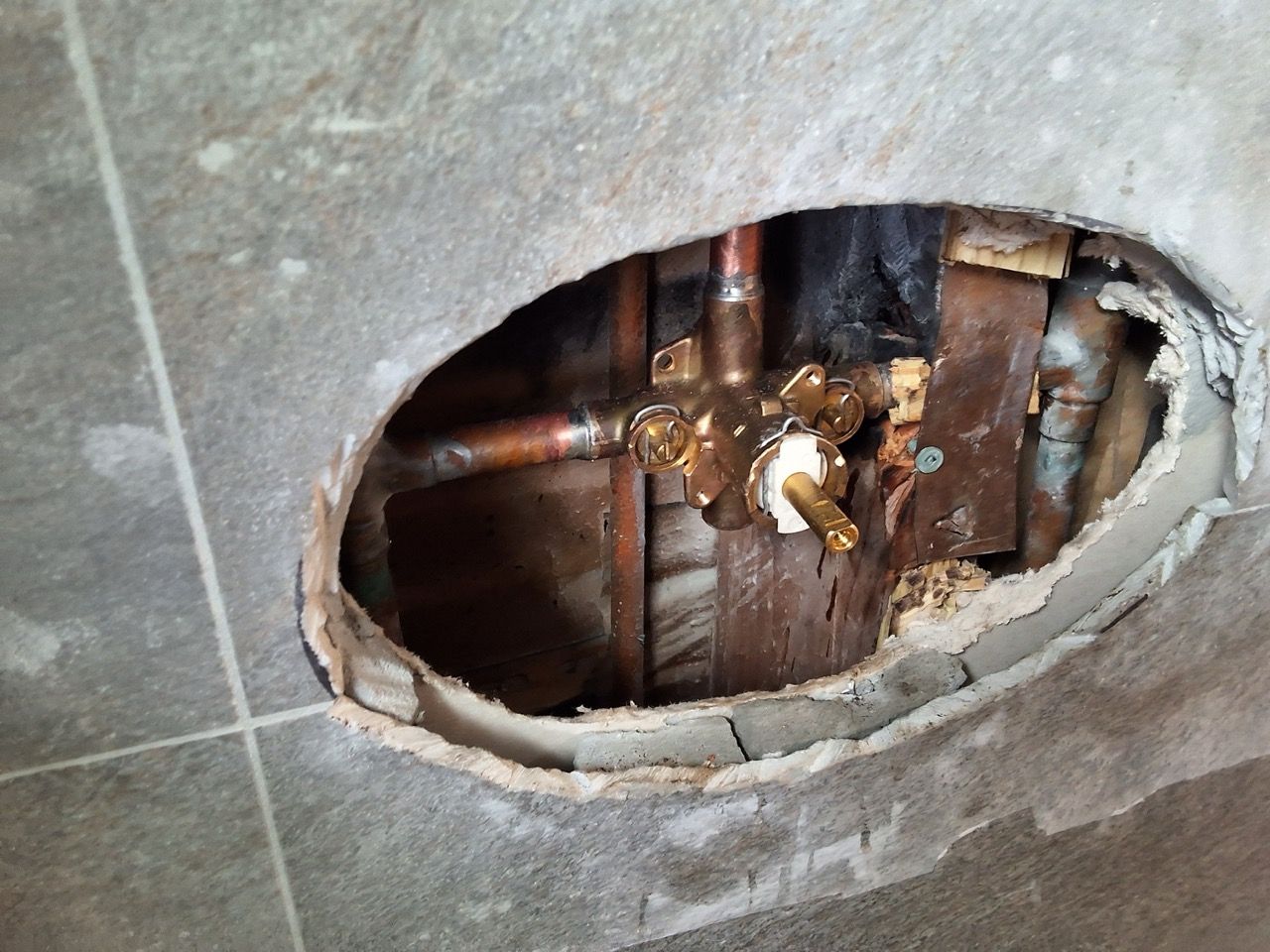 Broken wall tile exposing pipes and plumbing behind the wall