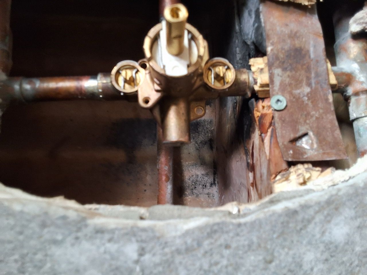 Close-up of a brass plumbing valve and pipe fittings inside a wall cavity