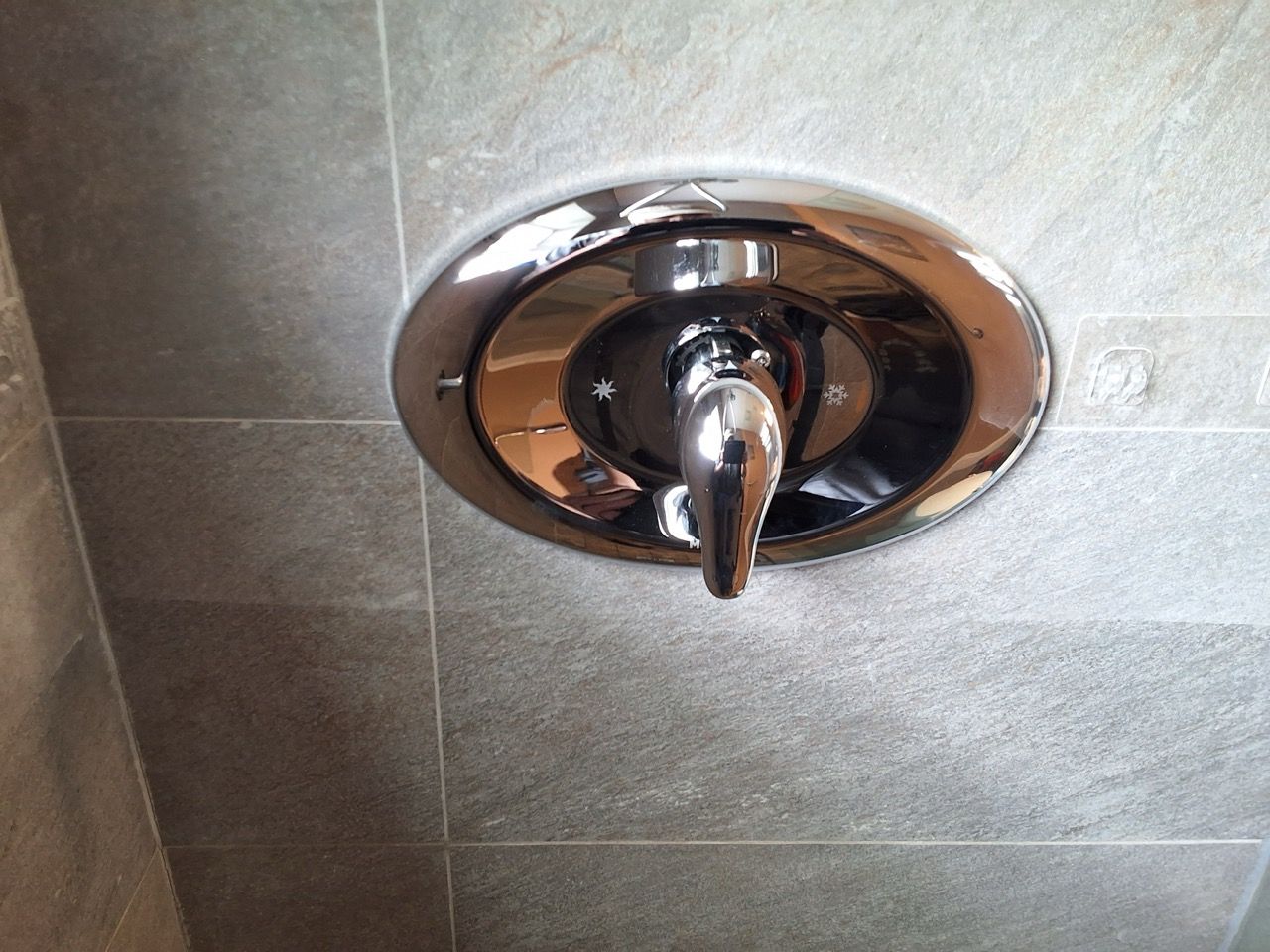 Chrome shower control knob on tiled bathroom wall