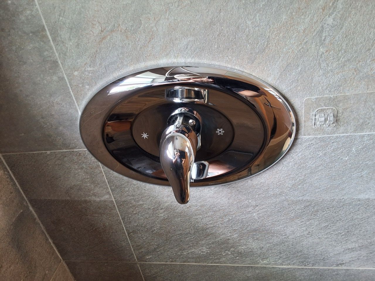 Chrome shower control knob on a tiled bathroom wall