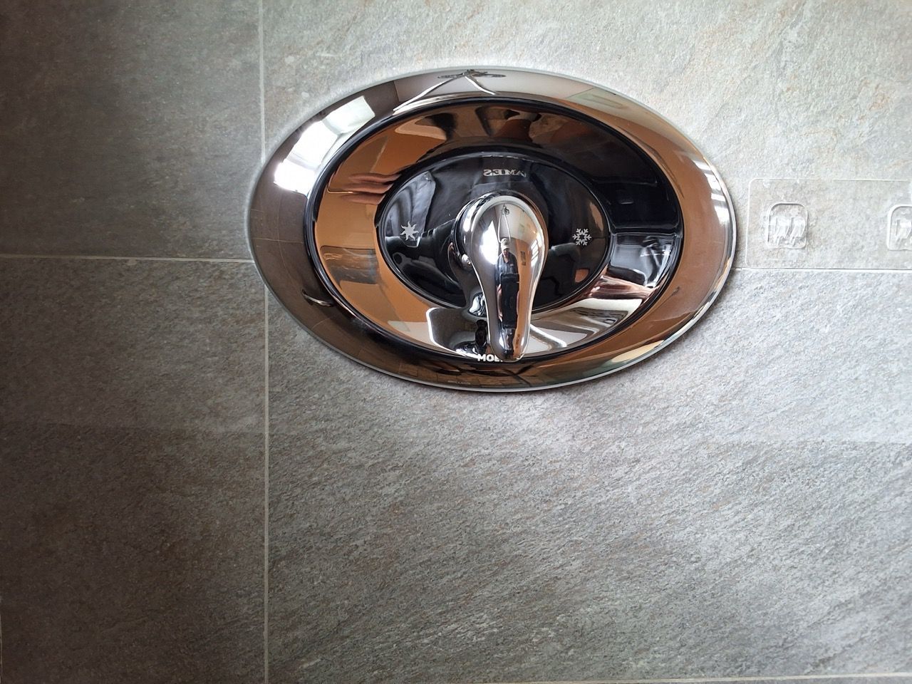 Chrome bathtub faucet handle on gray tiled wall